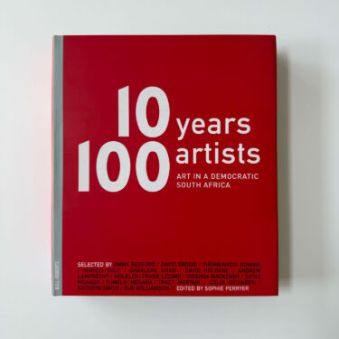 Red book cover with large white typography reading “10 Years 100 Artists: Art in a Democratic South Africa”